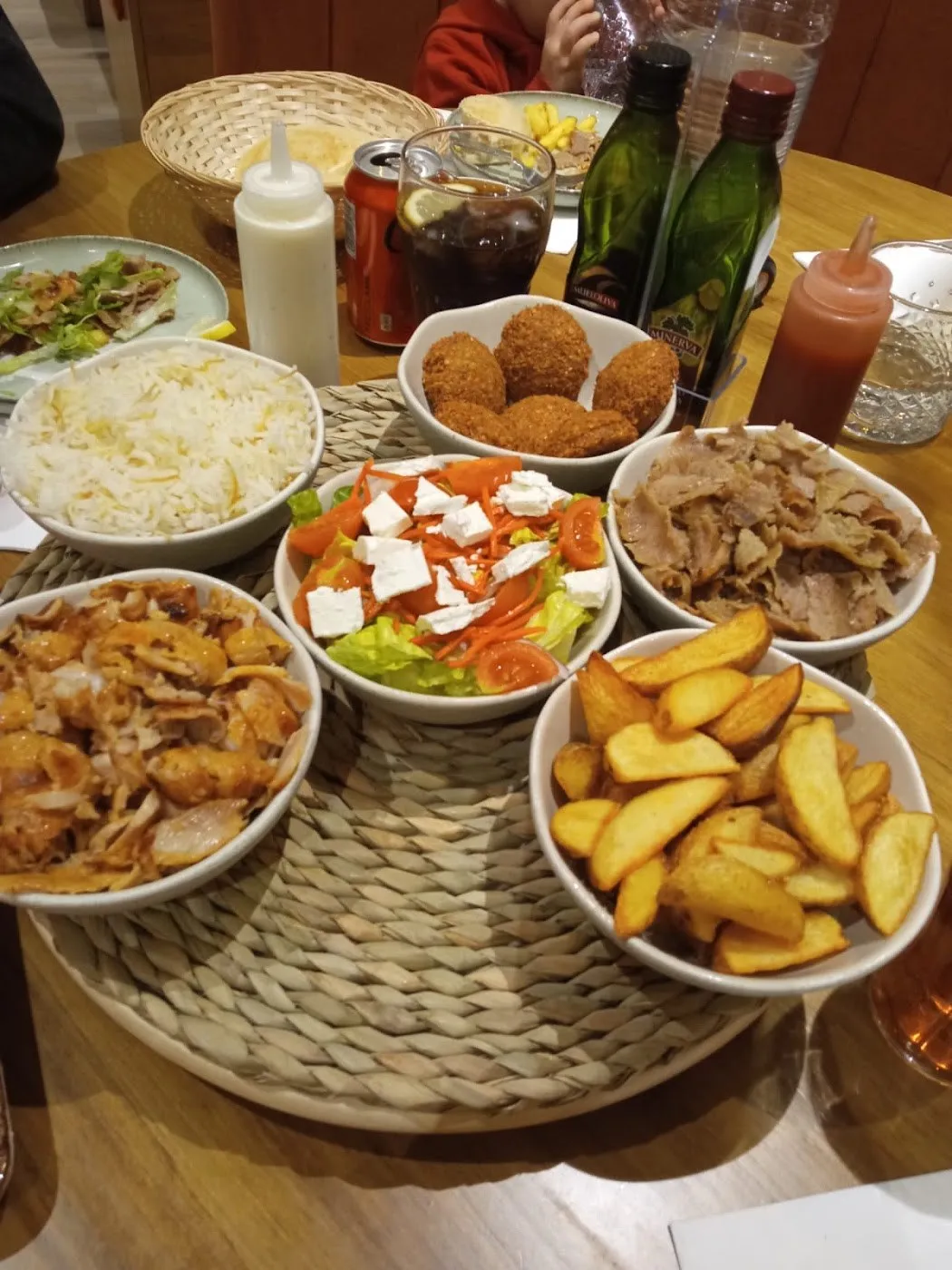 Mesa con cuencos de arroz, carne de kebab, falafel, patatas y ensalada griega