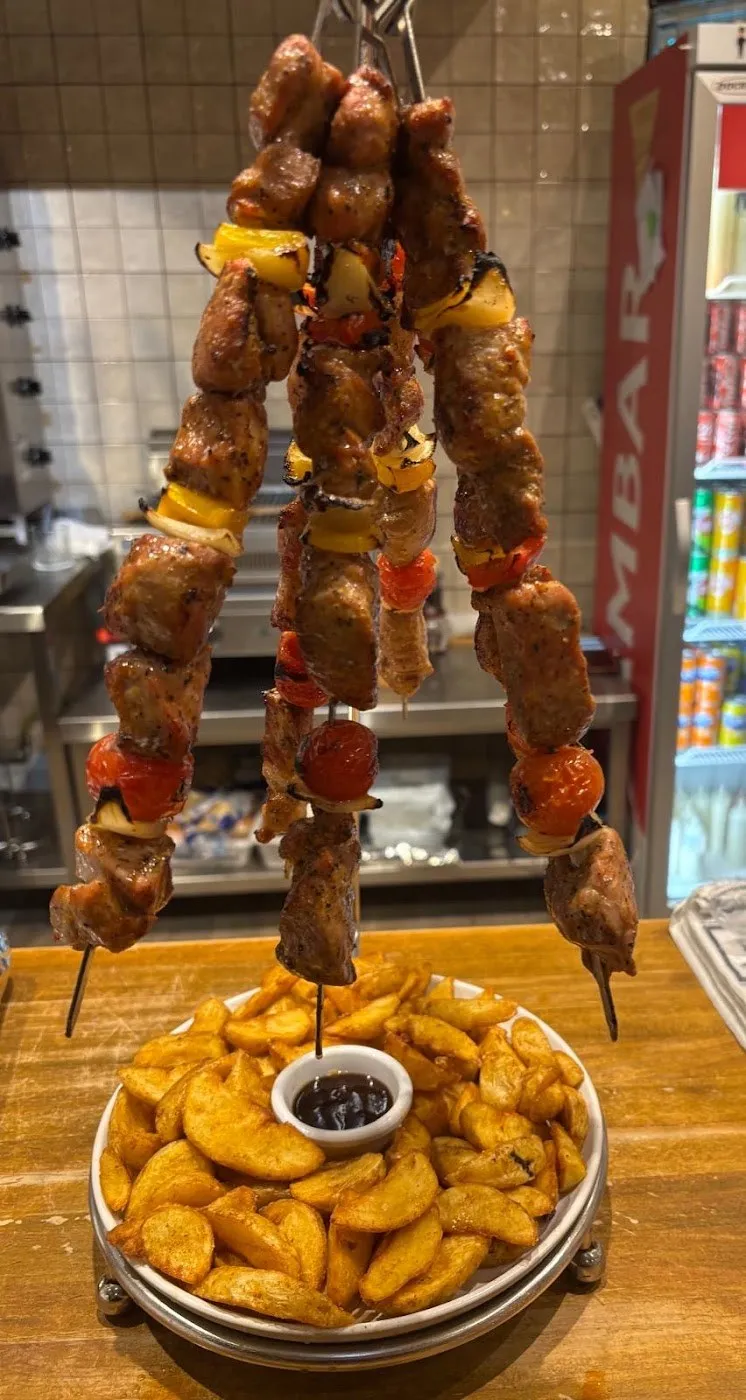 Brochetas colgadas sobre un plato de patatas gajo con salsa
