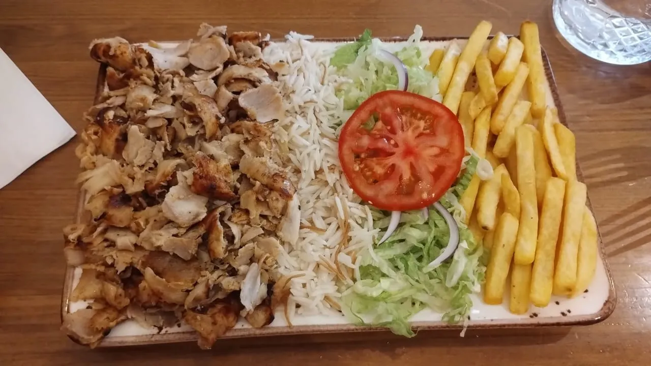 Plato de carne de kebab con arroz, ensalada, tomate y patatas fritas